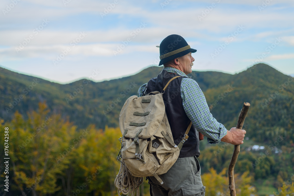 The old man stands on the top of the mountain and enjoys the view of the autumn mountains. An elderly man is an active and healthy lifestyle.

