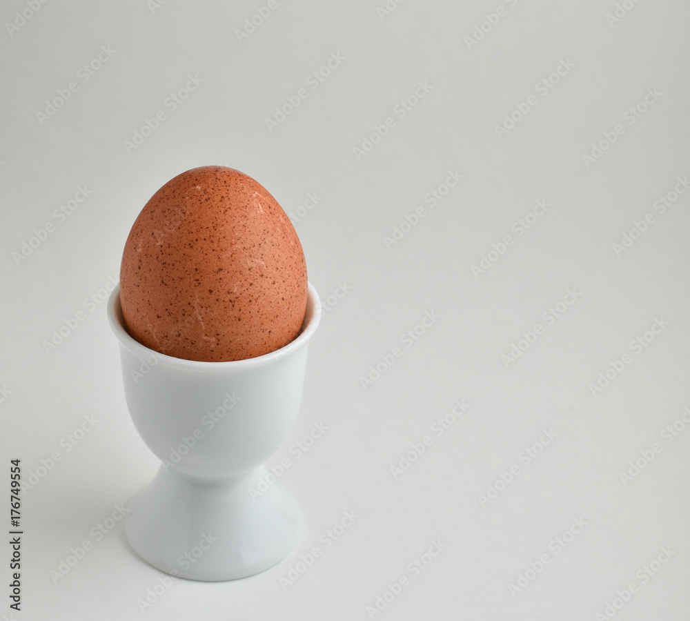 Speckled brown organic egg in white ceramic egg holder Speckled brown organic egg in white ceramic egg holder