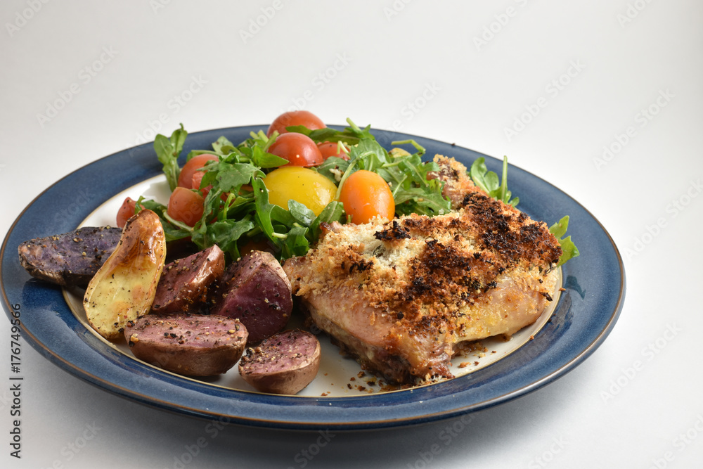 Healthy meal with roaster herb crusted chicken, multicolor fingerling potatoes, and arugula salad with heirloom tomatoes and lemon dressing.