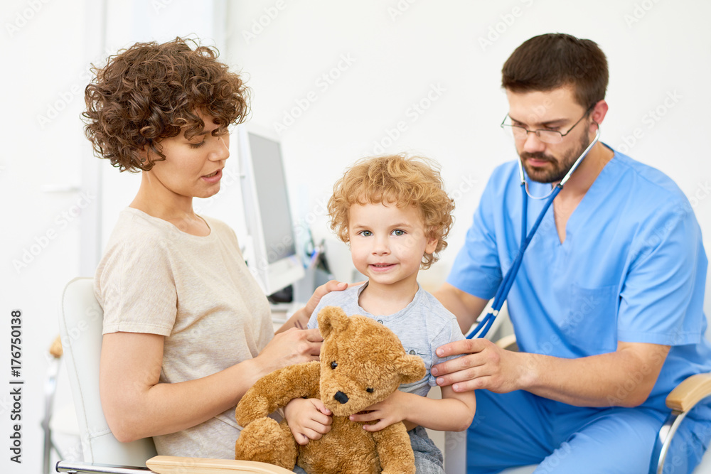 Φωτογραφία Portrait of happy little boy sitting on mothers lap in doctors office looking at