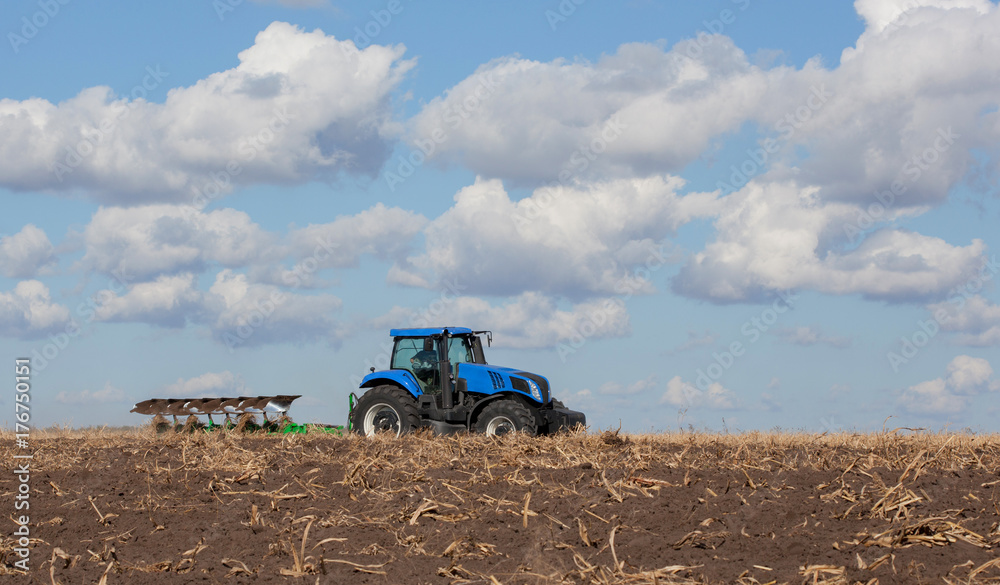 Naklejka premium a large blue tractor, plowing field against the beautiful sky. Work of agricultural machinery. Harvest