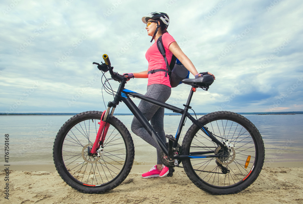 One young woman, an athlete in pink shoes, walks with a mountain bike in the morning on the river bank. One young woman, an athlete in pink shoes, walks with a mountain bike in the morning on the river bank.