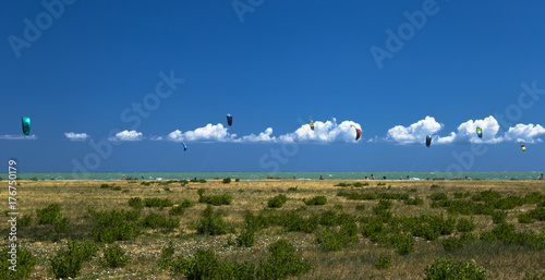 Panoramic view of kitesurfers sailing in a beach under beautiful clouds