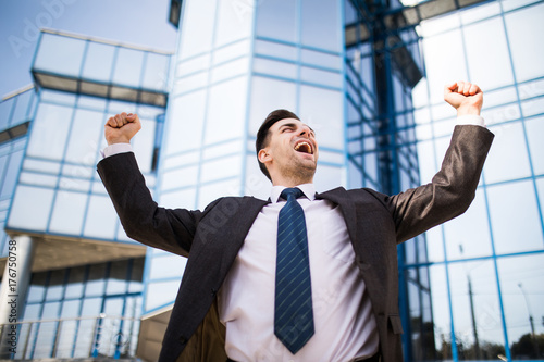 Handsome businessman raising arms in sign of victory outdoors against office building