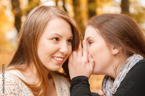 woman telling secret to her friend smiling