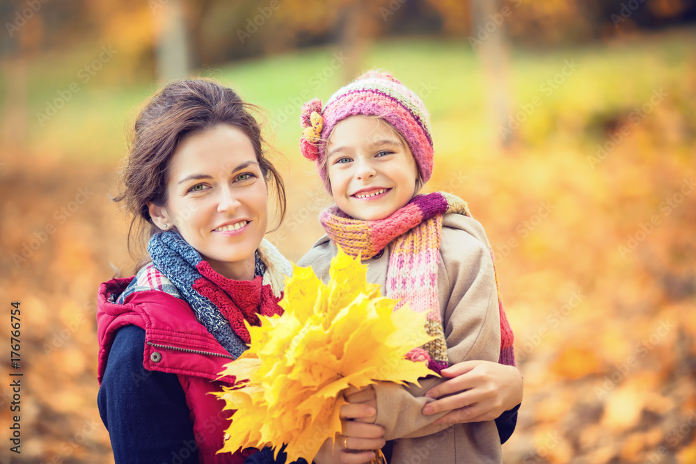 Smiling little girl and her mother enjoy walk in autumn park and play with bright autumn leaves Smiling little girl and her mother enjoy walk in autumn park and play with bright autumn leaves