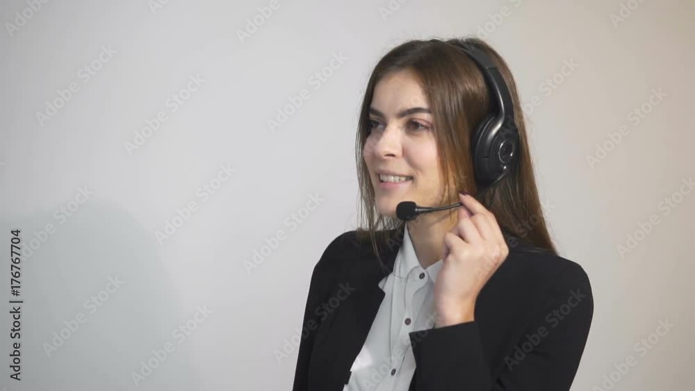 Smiling operator, in smart white blouse and black jacket, talking on the headset in the white background, indoor slowmotion Smiling operator, in smart white blouse and black jacket, talking on the headset in the white background, indoor slowmotion