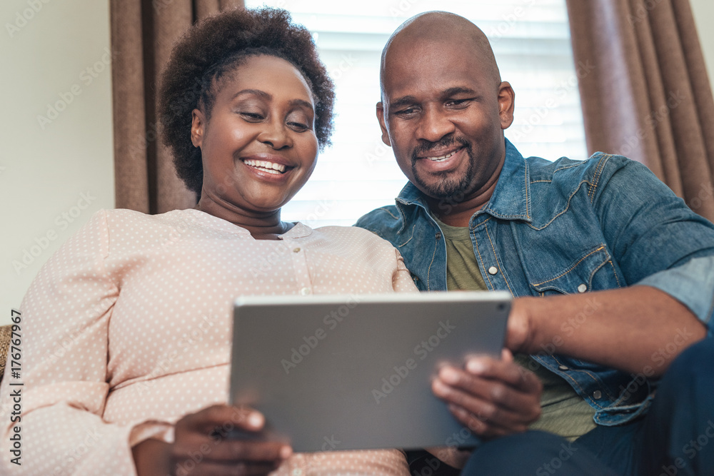 Smiling African couple sitting on a sofa using a tablet Smiling African couple sitting on a sofa using a tablet