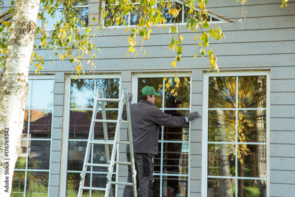 Φωτογραφία The worker makes painting of the facade of the wooden frame house after installation of windows