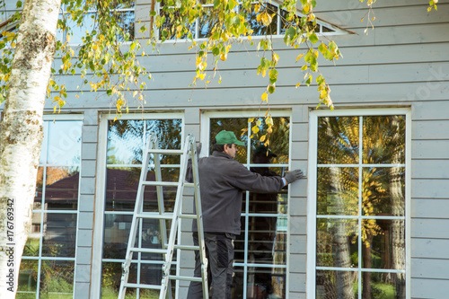 Canvas Print The worker makes painting of the facade of the wooden frame house after installation of windows