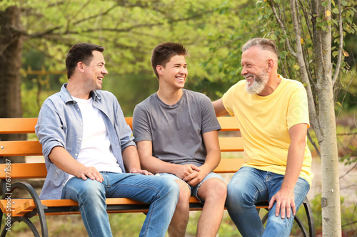 Teenager boy with dad and grandfather sitting on bench in park © Africa Studio