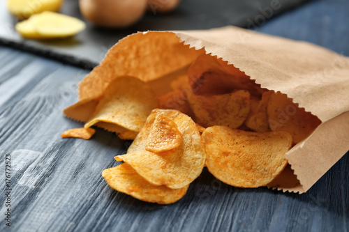 Paper bag with yummy crispy potato chips on wooden table