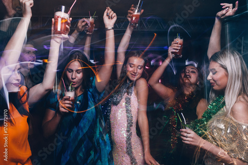 New Year dance party in night club. Happy friends company with drinks, Christmas celebration in motion. Disco people in blurred colors, modern youth life