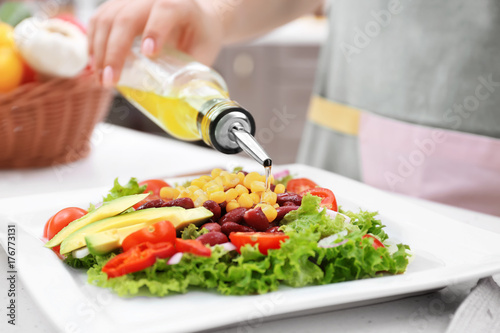 Woman pouring olive oil onto vegetable salad in kitchen