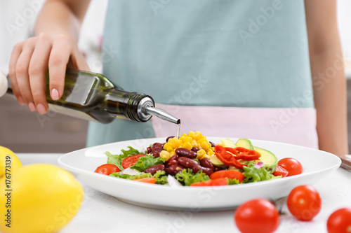 Fototapeta Naklejka Na Ścianę i Meble -  Woman pouring olive oil onto vegetable salad in kitchen