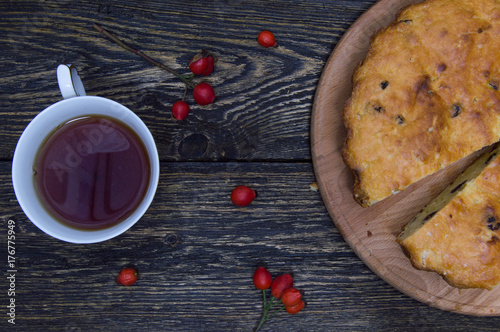 Homemade pie and cup tea with rosehip berries on grunge wooden background top view