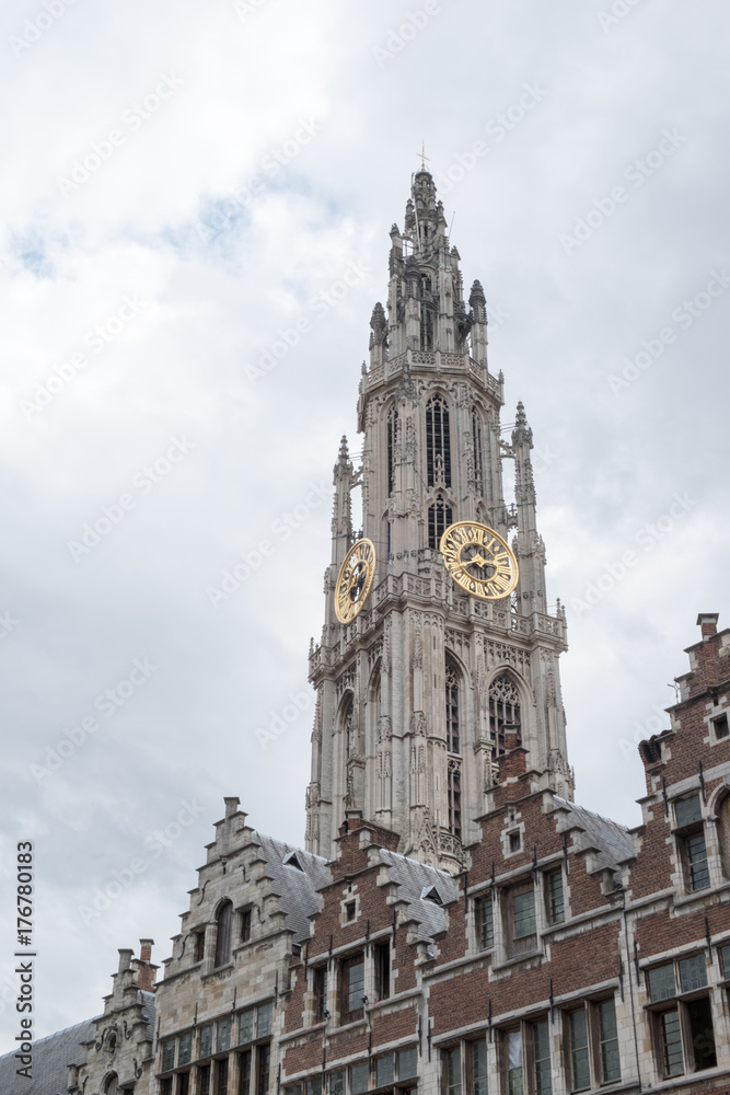 Onze-Lieve-Vrouwekathedraal (Cathedral of Our Lady) in Antwerp Belgium, Gothic Cathedral tower against an overcast sky. Dutch stepped gabled rooftop houses in foreground.