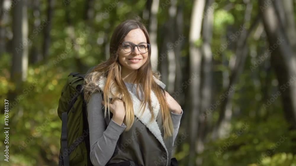 Intelligent tourist girl, with a green backpack, standing in the forest, slowmotion on sunny fall day Intelligent tourist girl, with a green backpack, standing in the forest, slowmotion on sunny fall day