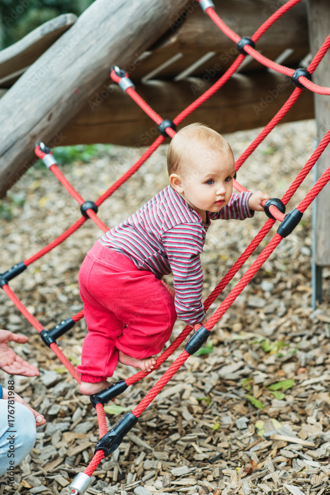 Adorable baby girl climbing the net on playground. 9-12 months old child having fun outdoors Adorable baby girl climbing the net on playground. 9-12 months old child having fun outdoors