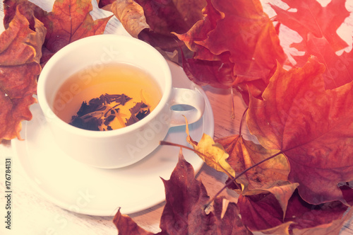 A cup of tea on a table that is strewn with fallen leaves. Warm autumn. Toning and blurring