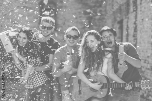 Group of happy friends having fun making a party on street playing guitar and listening music while throwing confetti - Concept of funny people friendship - Black and white edit - Defocused background