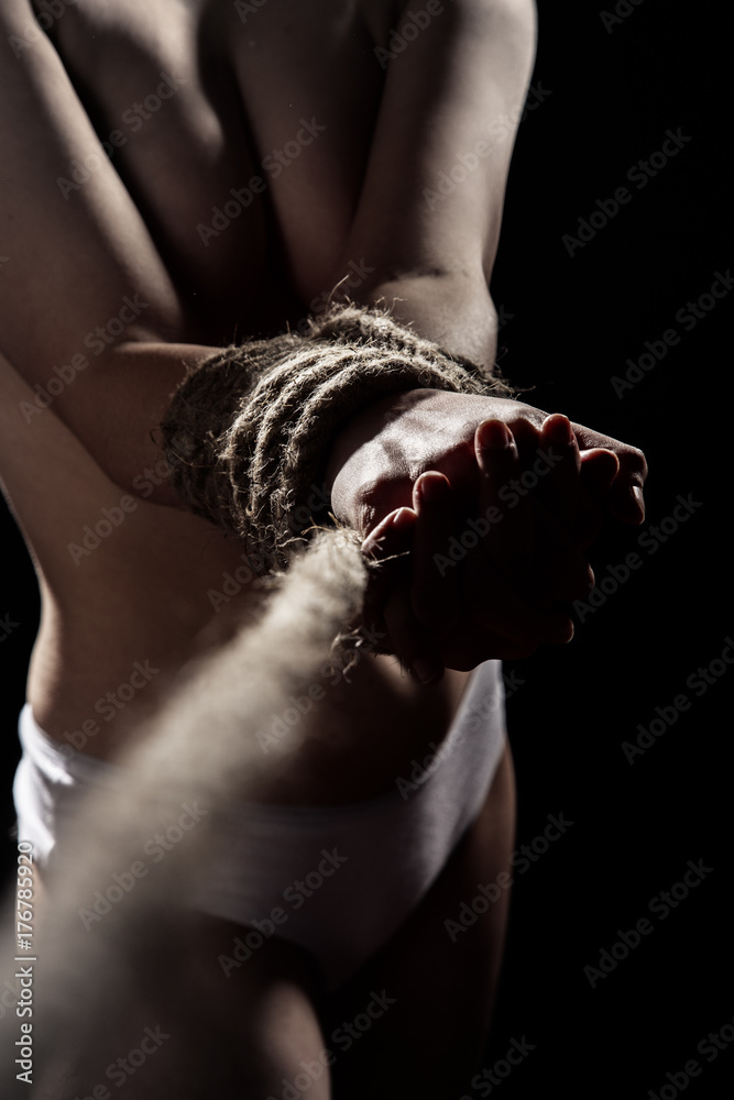 unrecognizable young naked woman with tied hands on black background