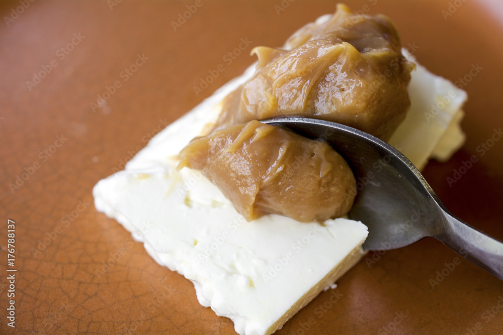 Closeup on spoon picking a serving of caramel cream (doce de leite) with white cheese (Queijo de Minas), a Brazilian desert, viewed from the side, on ceramic plate Closeup on spoon picking a serving of caramel cream (doce de leite) with white cheese (Queijo de Minas), a Brazilian desert, viewed from the side, on ceramic plate