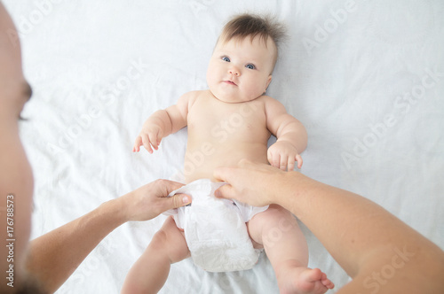 Dad changing diaper on baby girl on bed, changing nappy, everyday care. Top view.