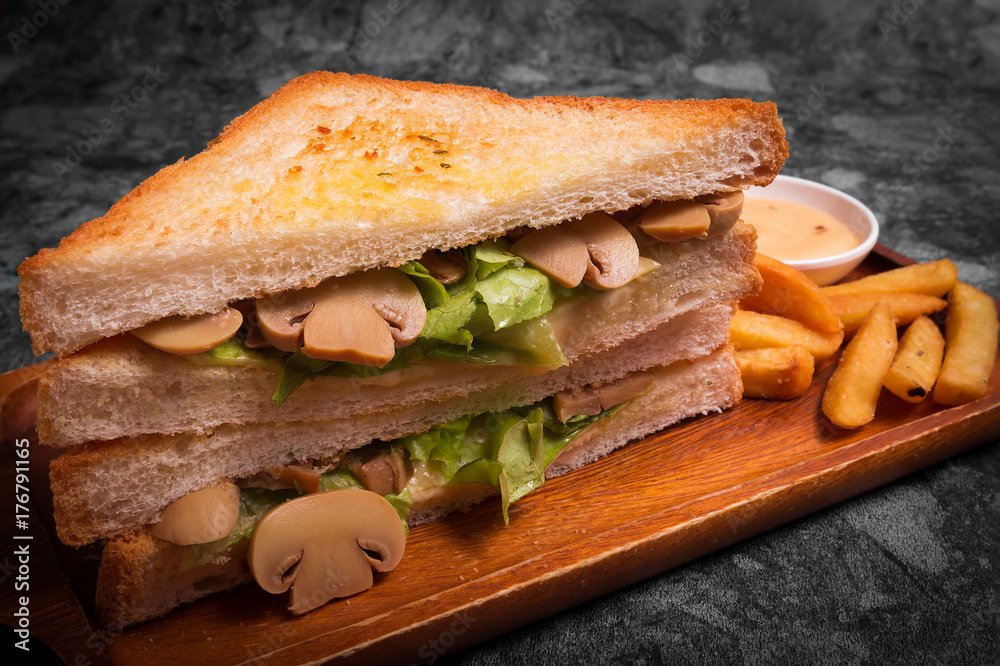 Tasty Sandwich with mushrooms serve with French fries and sauce on the wooden plate. Tasty Sandwich with mushrooms serve with French fries and sauce on the wooden plate.