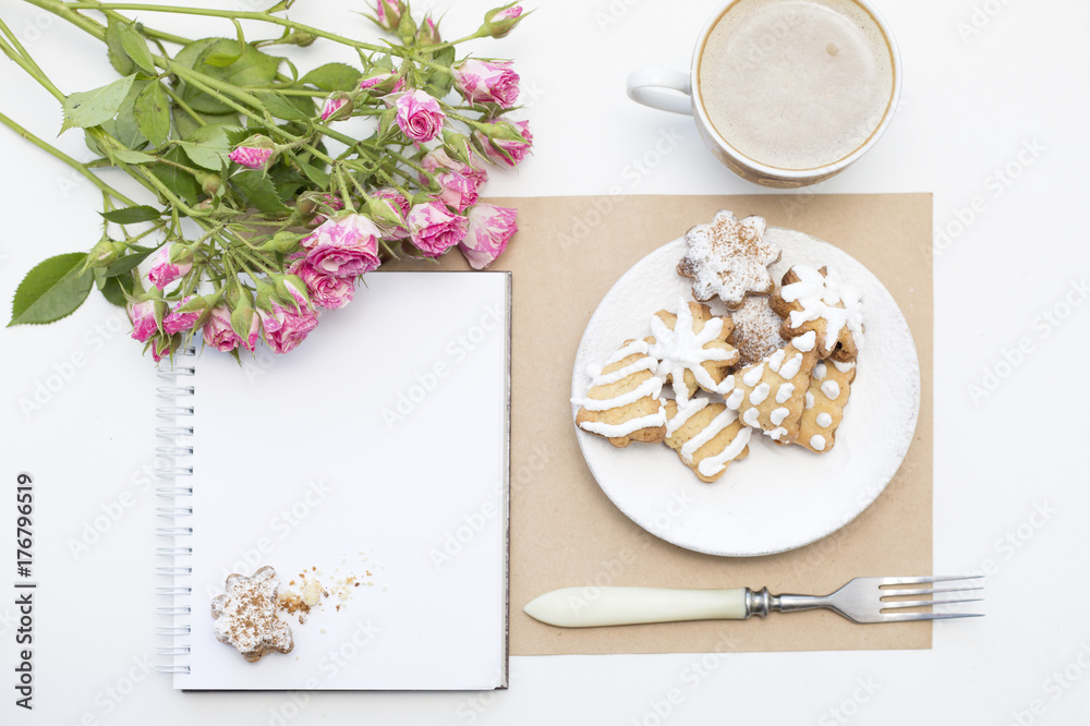 Mockup with blank notepad, cup of coffee and little garden pink roses. New year cookies and cappuccino. Christmas morning still life. Mockup with blank notepad, cup of coffee and little garden pink roses. New year cookies and cappuccino. Christmas morning still life.
