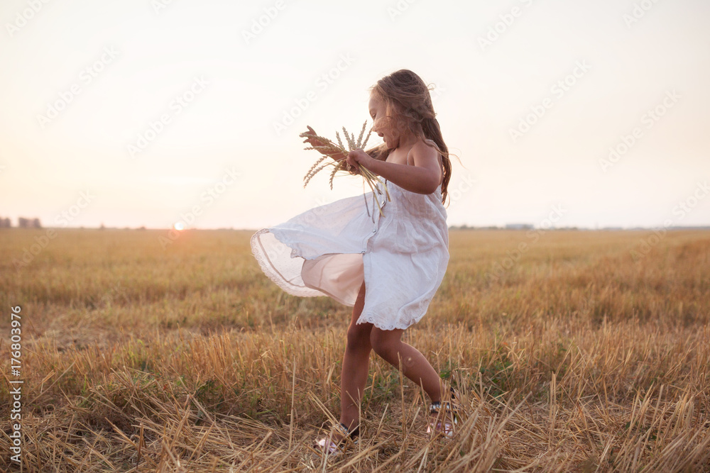 Little beautiful smiling girl on a gold wheat field walking at sunset ...