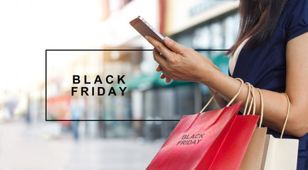 Black Friday, Woman using smartphone and carrying shopping bag while standing on the mall background