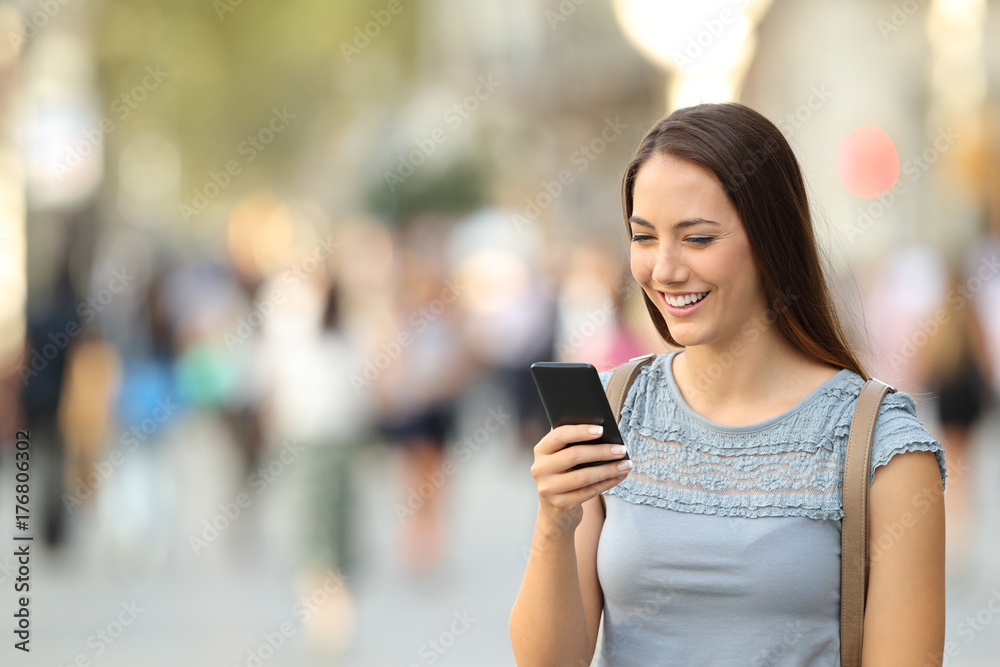 Happy lady using a smart phone standing on the street Happy lady using a smart phone standing on the street