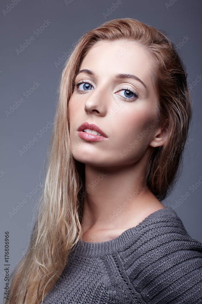 Portrait of young woman in gray woolen sweater. Beautiful girl posing on grey studio background. Female with blonde hair and day beauty makeup Portrait of young woman in gray woolen sweater. Beautiful girl posing on grey studio background. Female with blonde hair and day beauty makeup