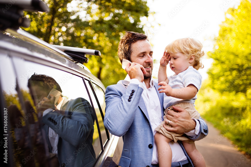 Young father with his little boy and smartphone at the car.