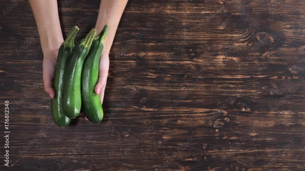 Unrecognizable woman holding vegetables over the wooden table. Close up female hands with zucchini Unrecognizable woman holding vegetables over the wooden table. Close up female hands with zucchini