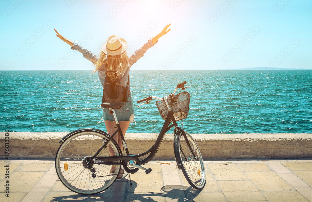 Blonde woman in summer hat with her bicycle walking coastline by Blonde woman in summer hat with her bicycle walking coastline by
