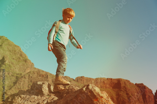 little boy with backpack hiking in mountains