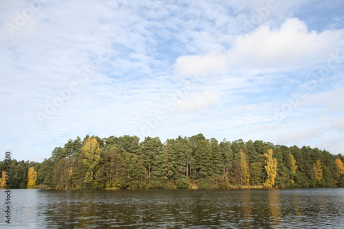 Farmside view of small countryside lake in the middle of forest in autumn.