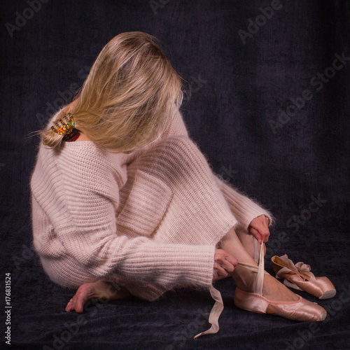 Ballet dancer sitting on the floor and puts on ballet shoes