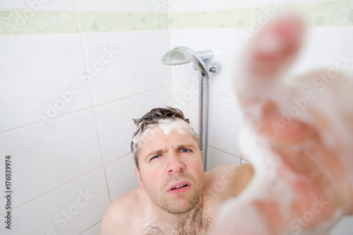 Fotografie A young caucasian man takes a shower and notices a hidden camera.