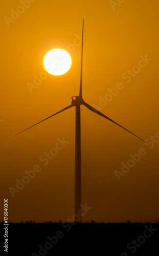 Silhouette of an isolated wind turbine at sunset with foggy and misty weather photo