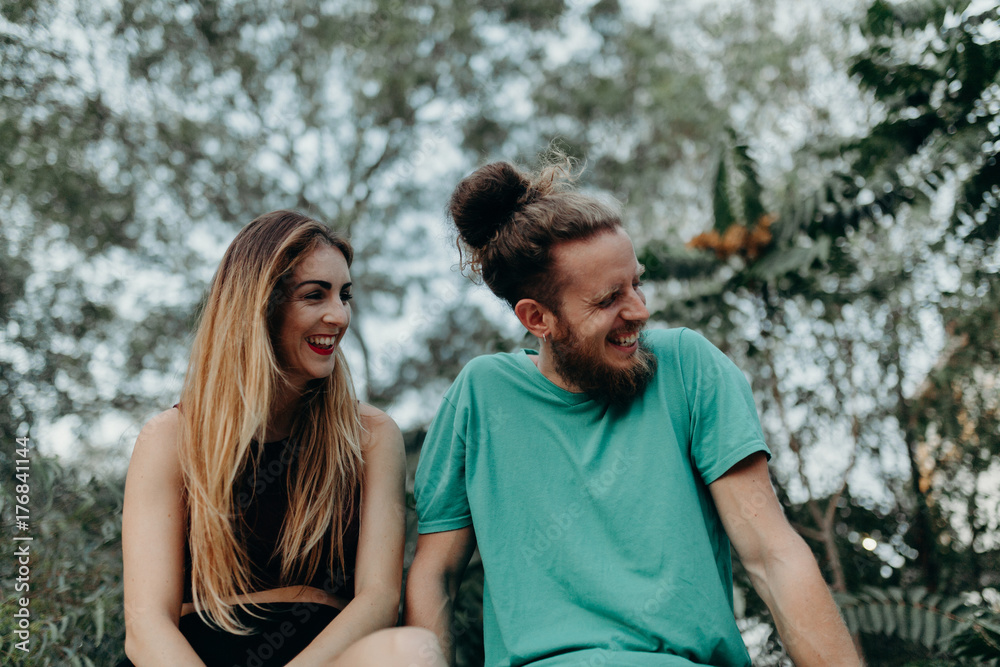 Happy alternative couple laughing together while sitting in nature