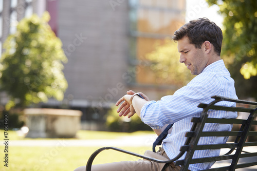 Businessman Sitting In City Park Looking At Smart Watch