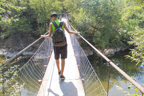 Eco tourism and healthy lifestyle concept. Young hiker boy with backpack. Traveler travel on the suspension bridge go trekking together