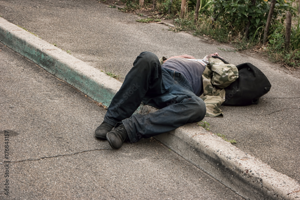 Unconscious drunk man. Person lying in the street. Health problems of the homeless. - obrazy, fototapety, plakaty 