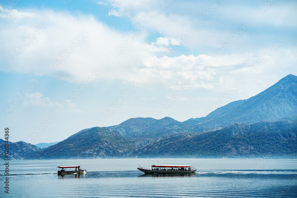 Boats are crossing tranquil lake with mountains landscape. Amazing view at Skadar lake, Montenegro