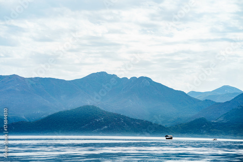 Amazing view on tranquil lake water and mountains landscape, boats in a distance. Skadar lake, Montenegro © GolubaPhoto