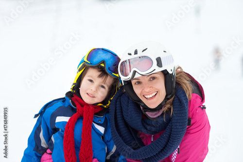Sweet young boy and his mother, learning to ski on a mild ski slope in Austrian ski resort