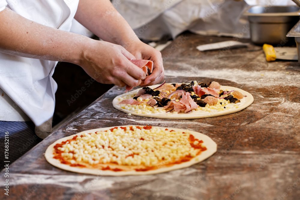 Cook putting toppings on two pizzas.